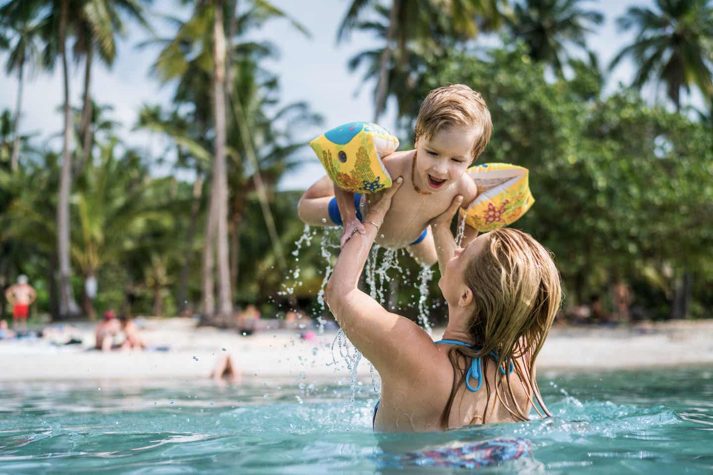 Eine Frau mit Kind im Meer. Im Hintergrund sind Palmen zu sehen