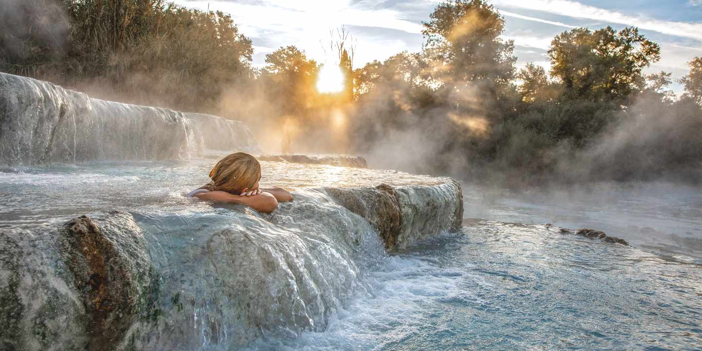 Frau genießt den Sonnenuntergang in einer Naturtherme in der Toskana im Wellessurlaub in italien