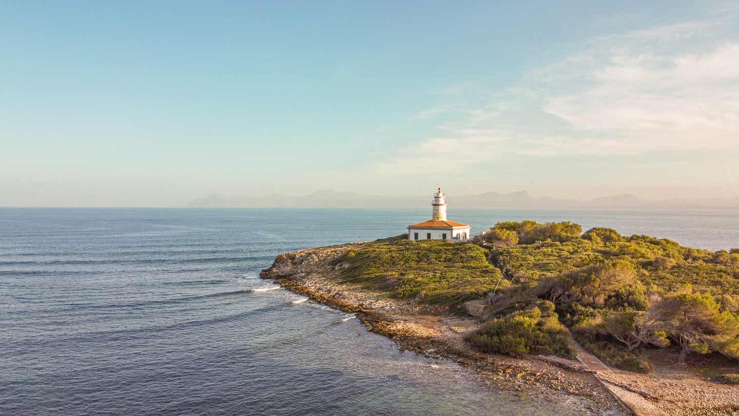 Weißer Leuchtturm mit eckigem Häuschen auf einer Landzunge von Meer umgeben