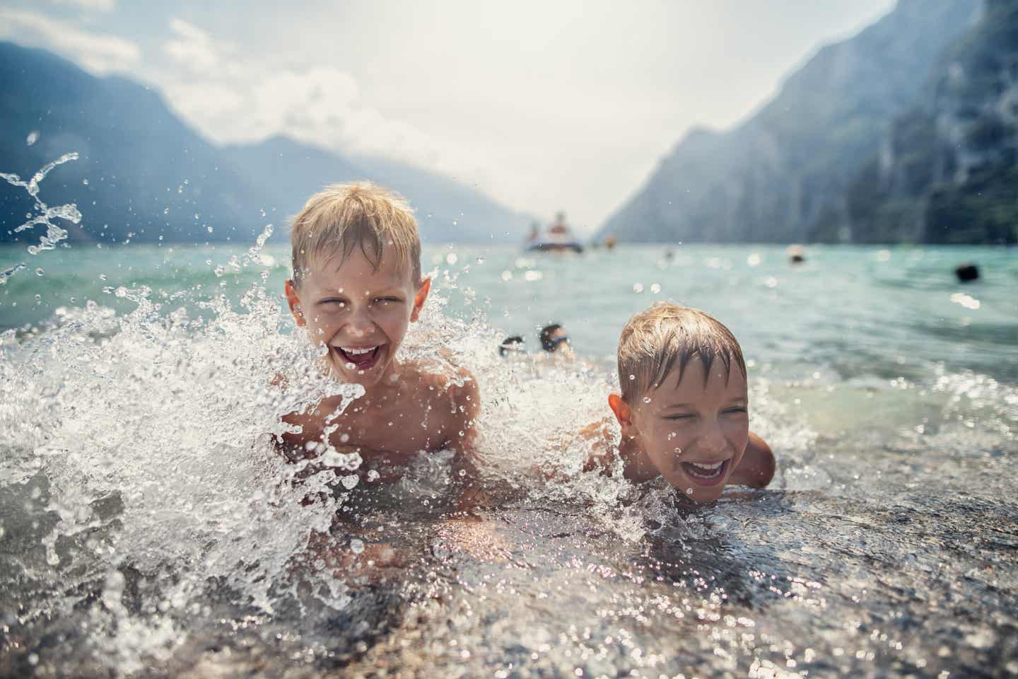 Gardasee Urlaub mit DERTOUR. Zwei Jungen spielen lachend im Wasser am Ufer des Gardasees