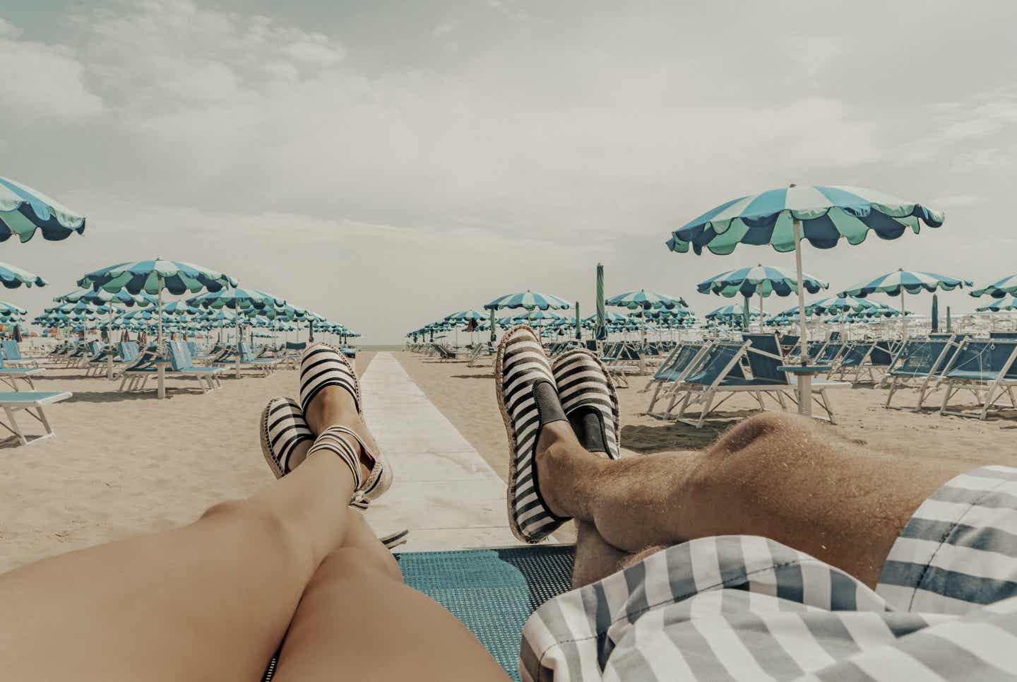 Rimini Urlaub mit DERTOUR. Füße eines Paares, das entspannt an einem Strand Riminis liegt und auf das Meer blickt