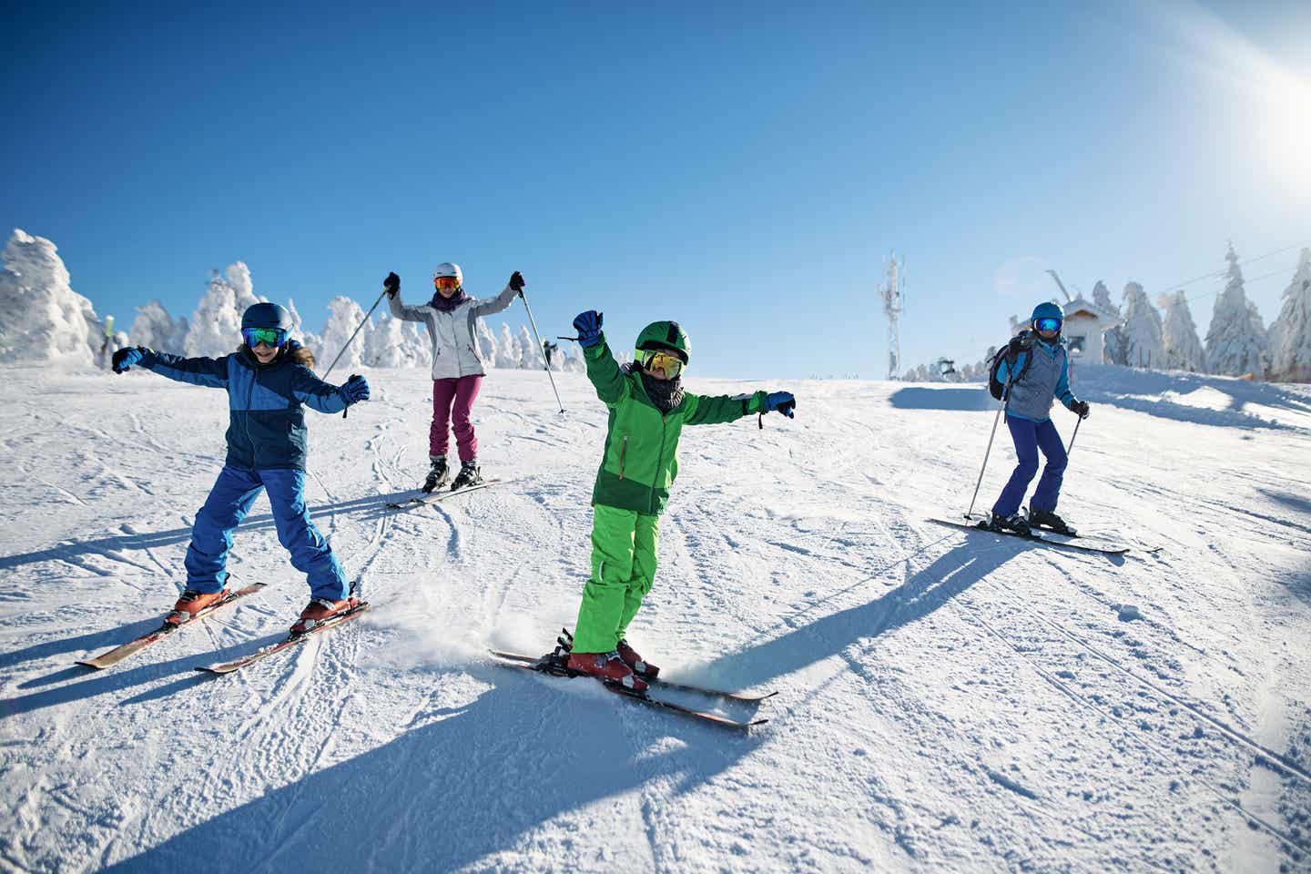 Vier Familienmitglieder fahren bei gutem Wetter auf der Skipiste