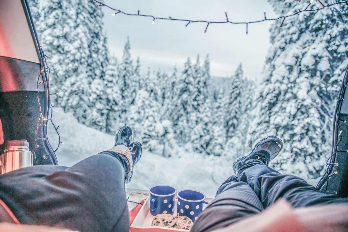 Erzgebirge Urlaub mit DERTOUR. Paar liegt mit den Füßen voraus im Kofferraum eines Kombis und blickt auf verschneite Landschaft