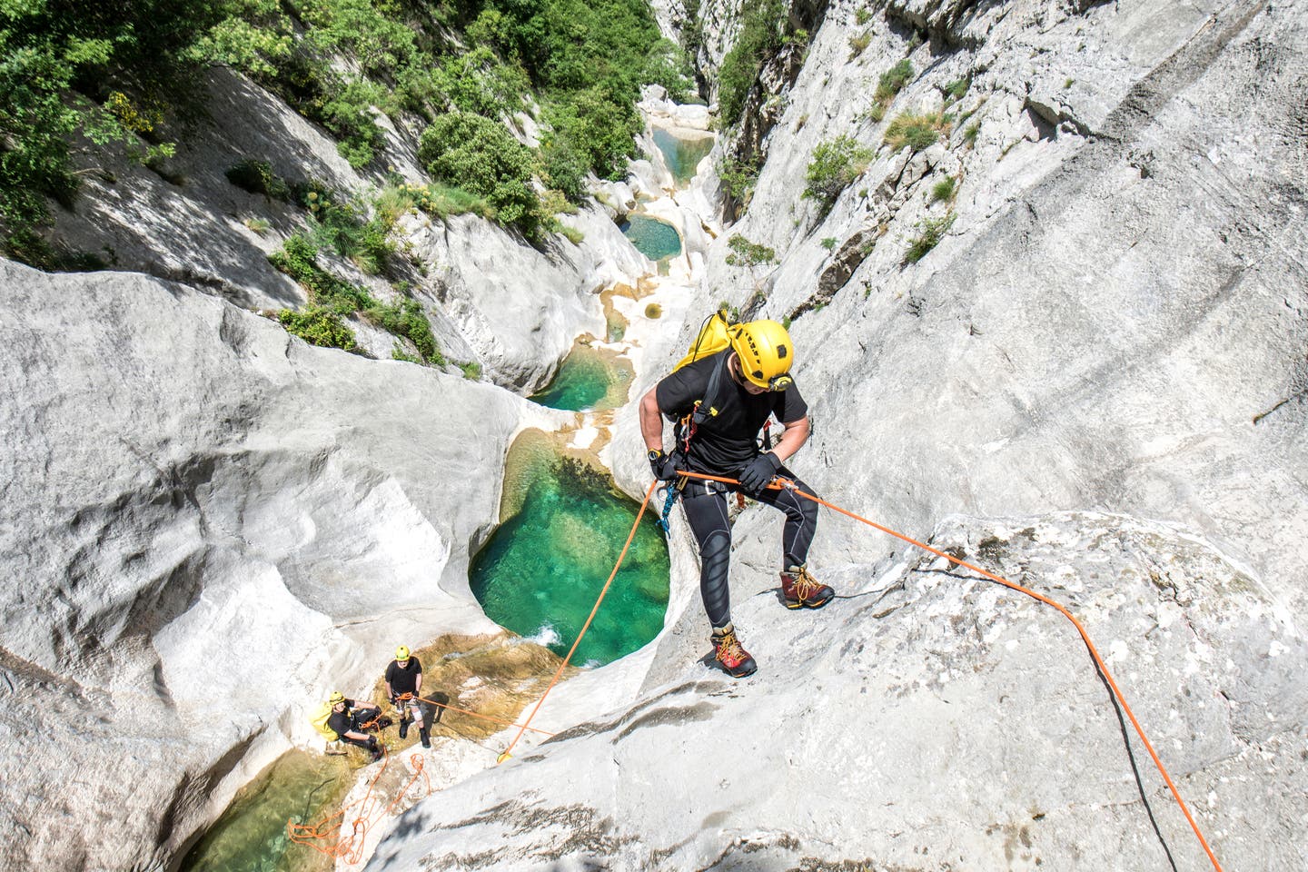 Mann klettert angeseilt eine Felsspalte mit Wasser hinab, Canyoning