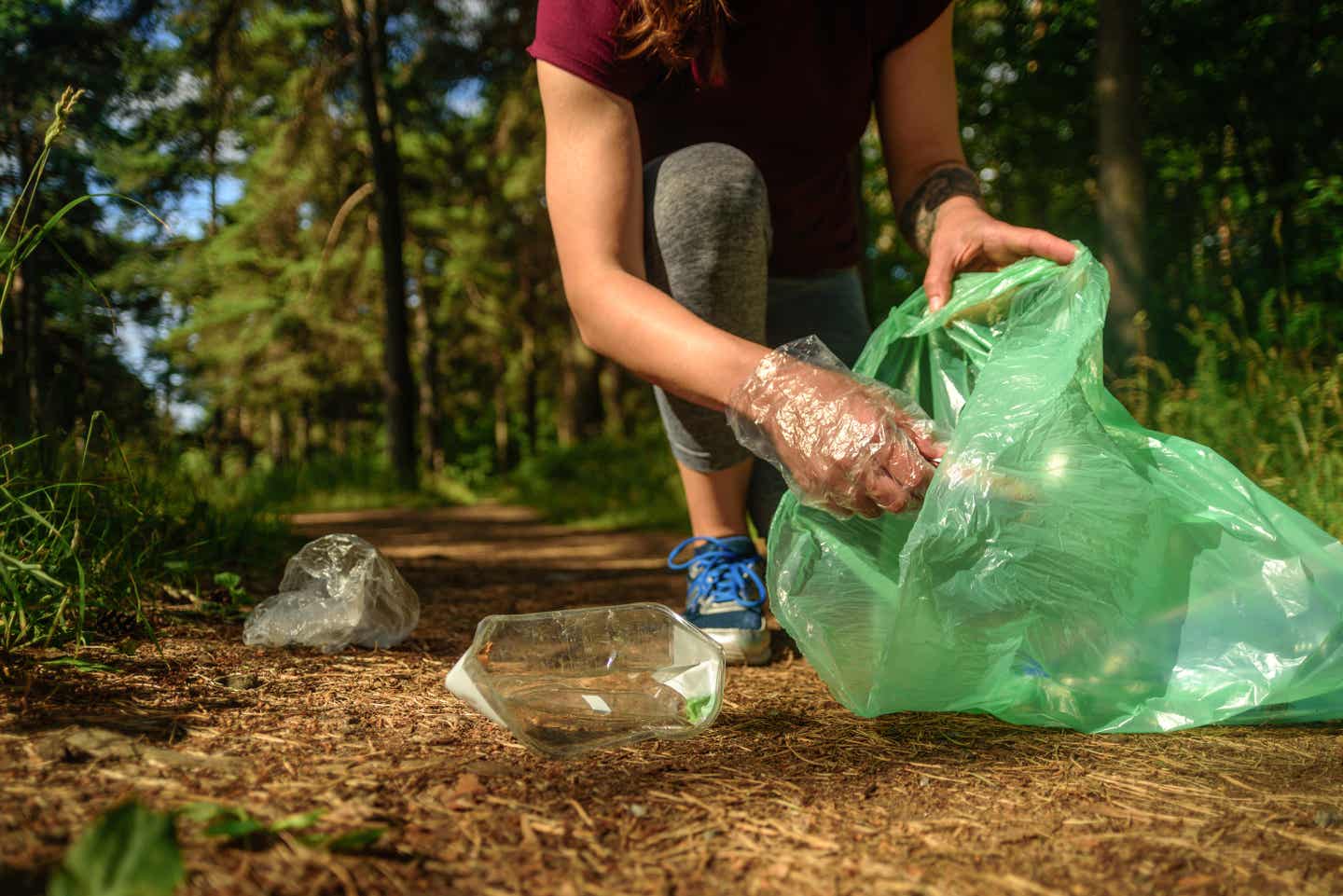 Frau sammelt im Wald mit Handschuhen Müll beim Joggen auf