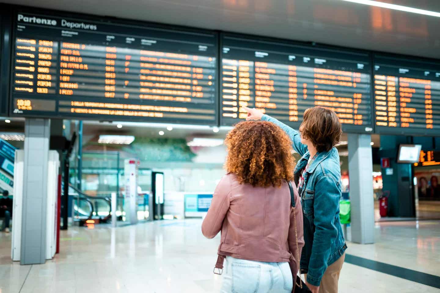 Reiseziele September. Pärchen am Flughafen vor der Abflugtafel.