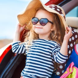 familienrundreise-maedchen-mit-sonnenbrille-und-hut-sitzt-im-kofferaum-g-1283486953.jpg
