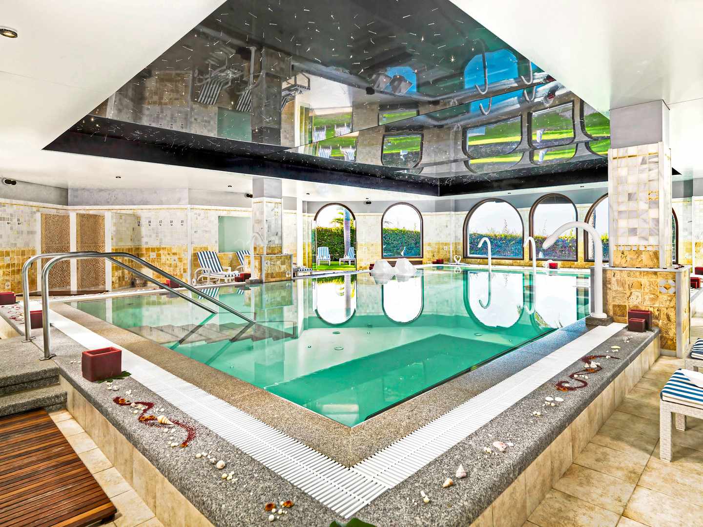 Im Pool dieses besten Wellnesshotels badest du in Ruhe Indoor-Poolbereich mit spiegelnder Decke und Liegen