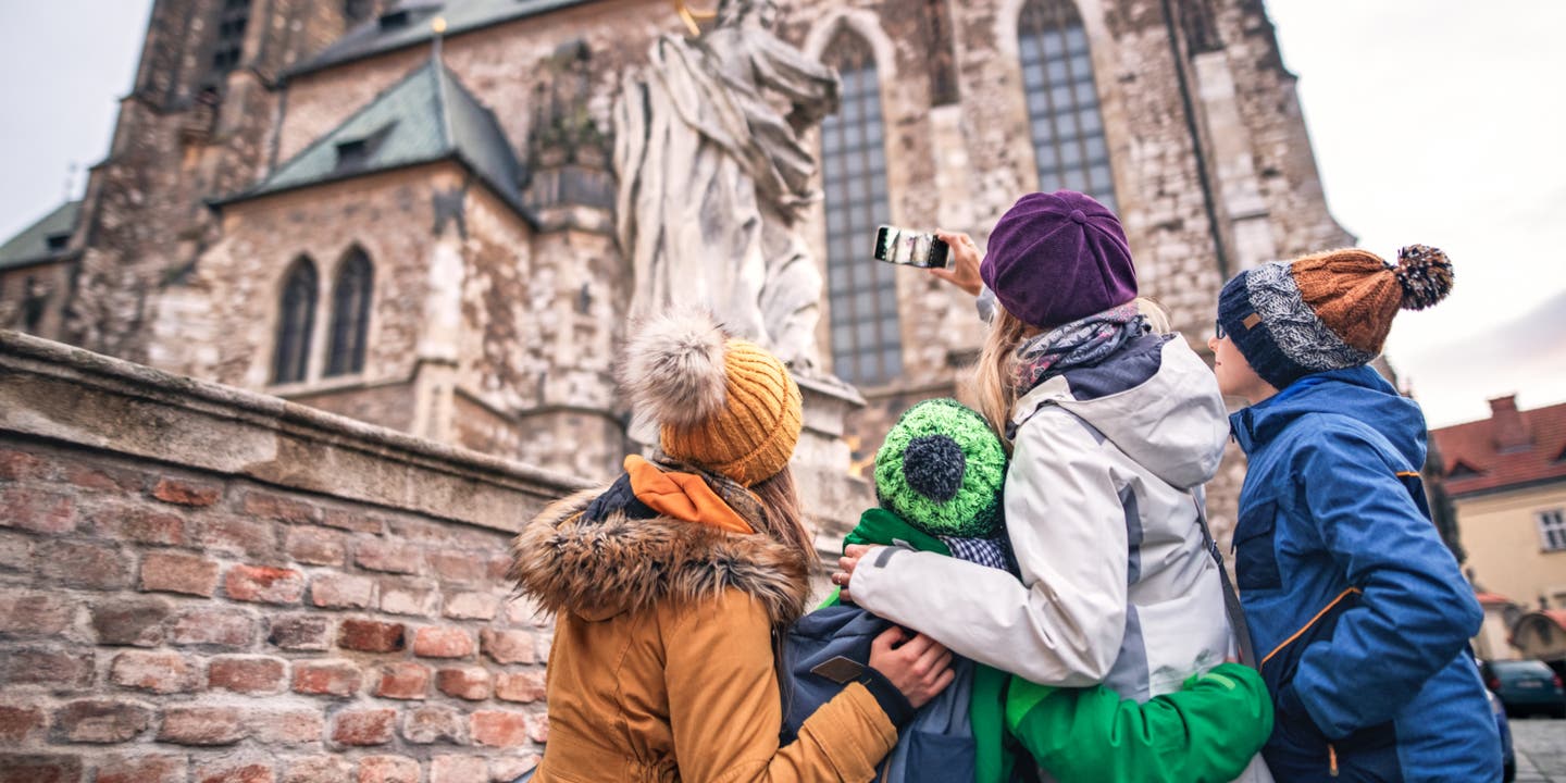 Frau mit drei Kindern mit dem Rücken zur Kamera vor großer Kathedrale
