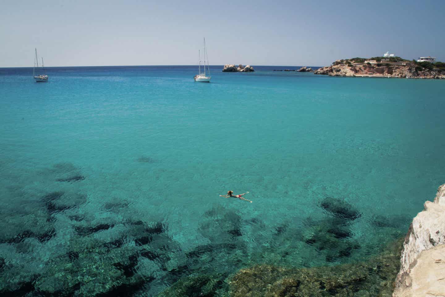 Karpathos Urlaub mit DERTOUR. Schwimmerin und Segelboote im klaren türkisen Wasser vor Karpathos