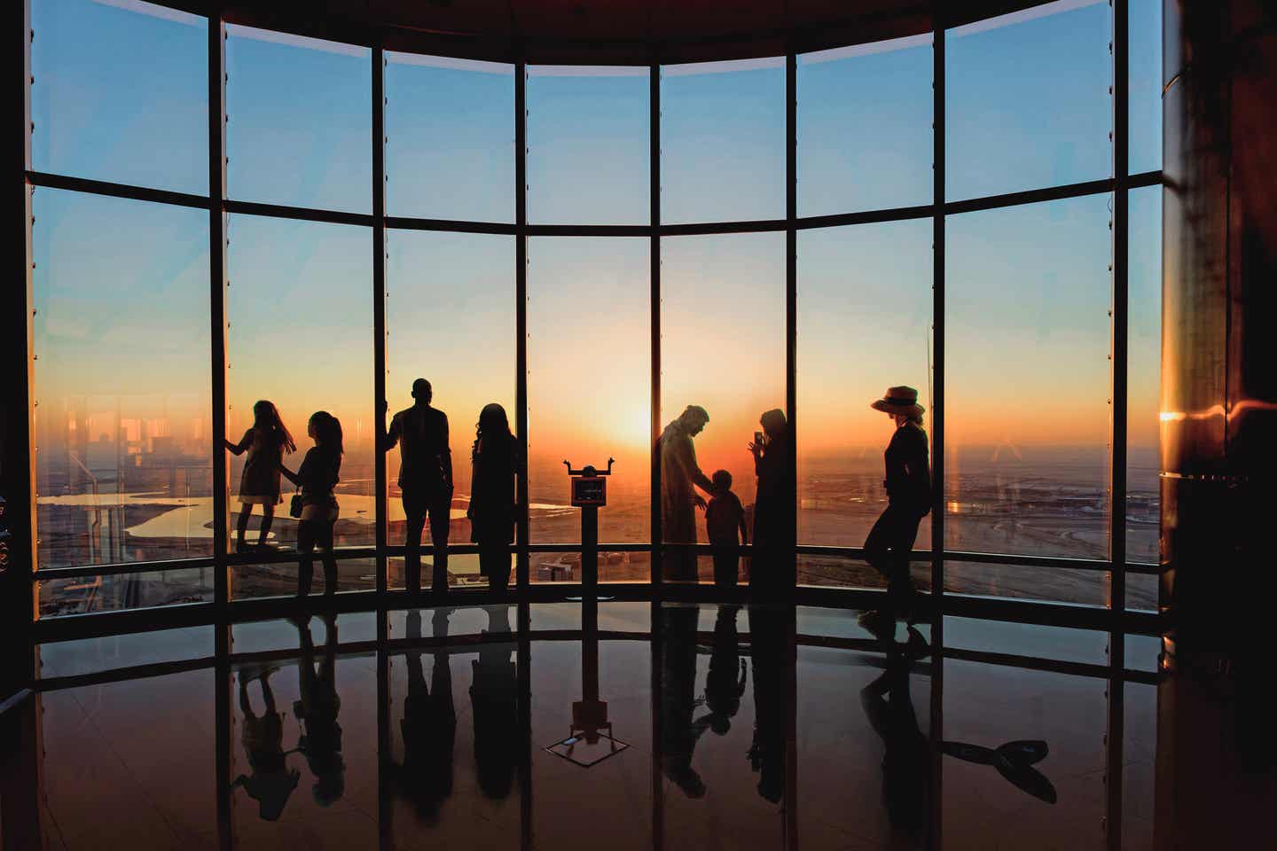 Mehrere Besucher auf einer Aussichtsplattform des Burj Khalifa, im Hintergrund ein Sonnenuntergang