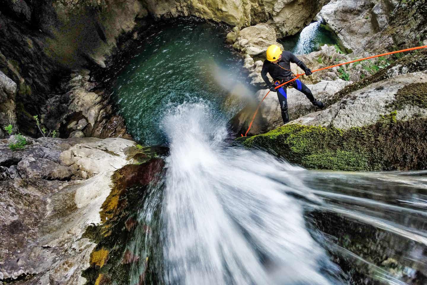 Mann seilt sich gesichert an einem Felsen in eine Schlucht voller Wasser ab