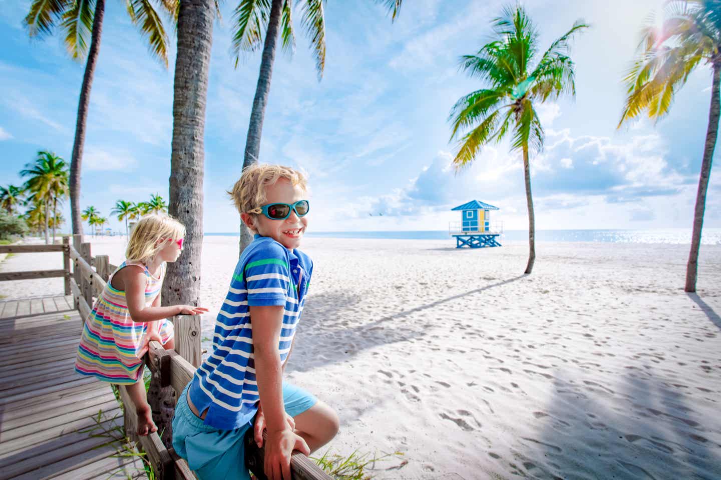 Ein Mädchen und ein Junge in bunter Kleidung und mit Sonnenbrillen schauen auf einen Strand in Florida