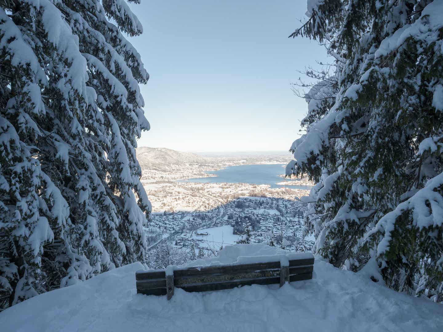 Tegernsee Urlaub mit DERTOUR. Fernblick von einer eingeschneiten Bank im Wald über dem Tegernsee