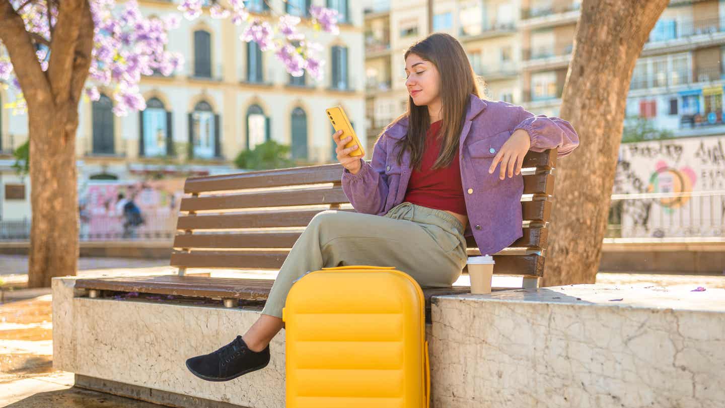 Reisende mit Koffer und Smartphone am sonnigen Platz in Málaga – idealer Startpunkt für einen Andalusien-Urlaub.