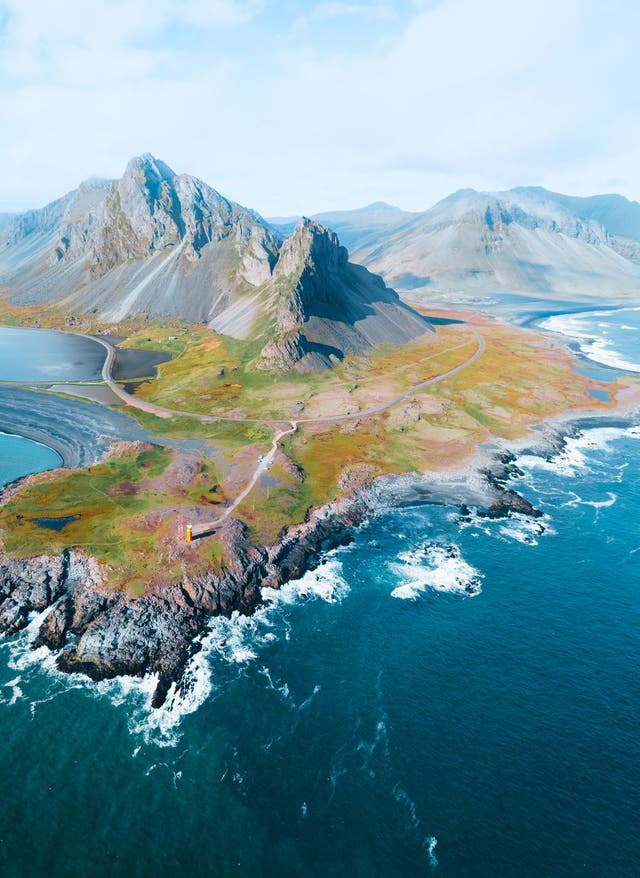 Island Urlaub Luftaufnahme von einer beeindruckenden Island Landschaft mit zerklüfteter Küste, tiefblauem Meer und markanten Bergen im Hintergrund