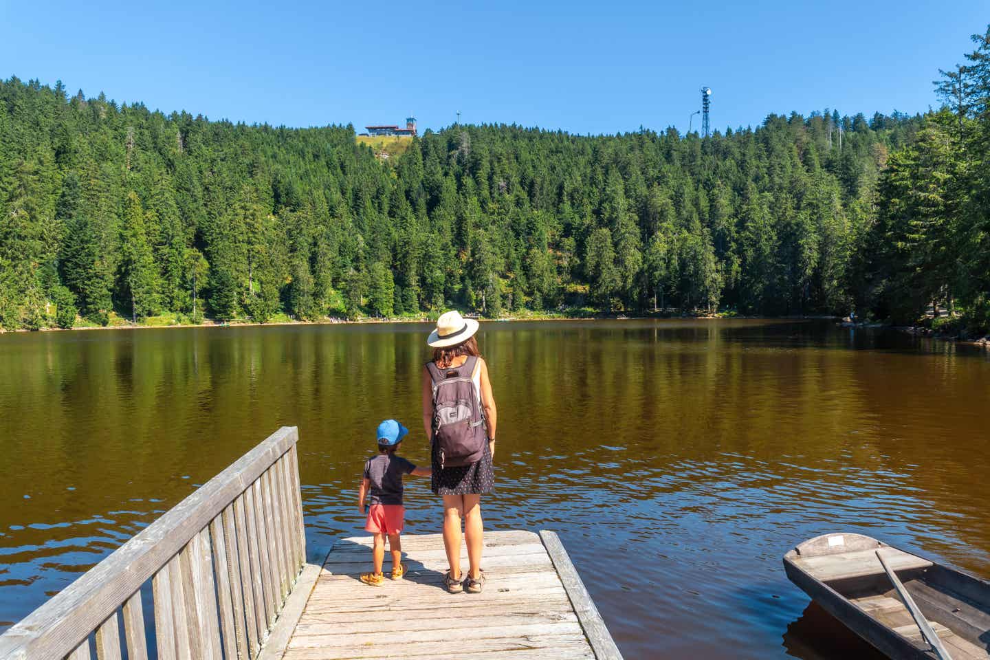 Eine Mutter steht mit ihrem Sohn auf einem Steg im Mummelsee; im Hintergrund sind die dichten Wälder des Schwarzwalds zu sehen