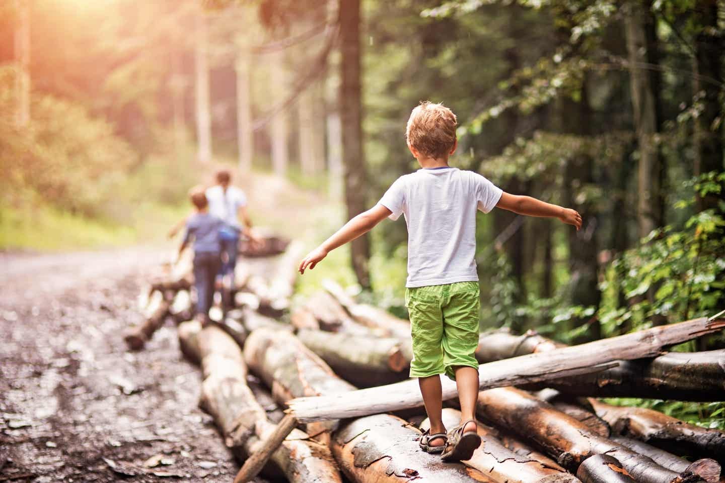 Kinder balancieren im Familienurlaub auf Baumstämmen im Wald.