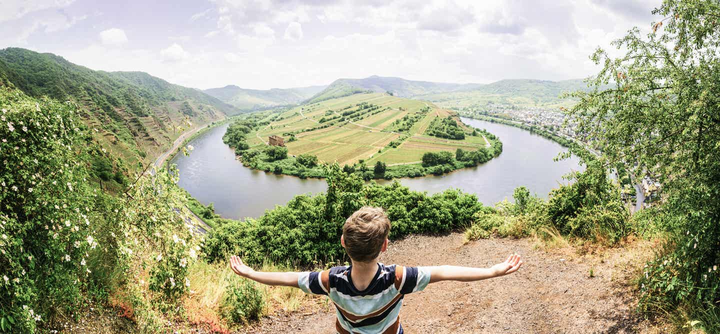 Mosel Urlaub mit DERTOUR. Kind streckt die Arme oberhalb der Moselschleife aus.