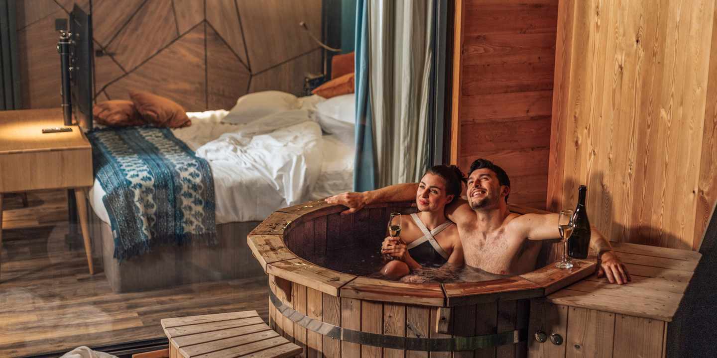 Paar entspannt während eines Wellnessurlaubs für Paare im beheizten Badezuber einer Berghütte mit Blick auf die Natur