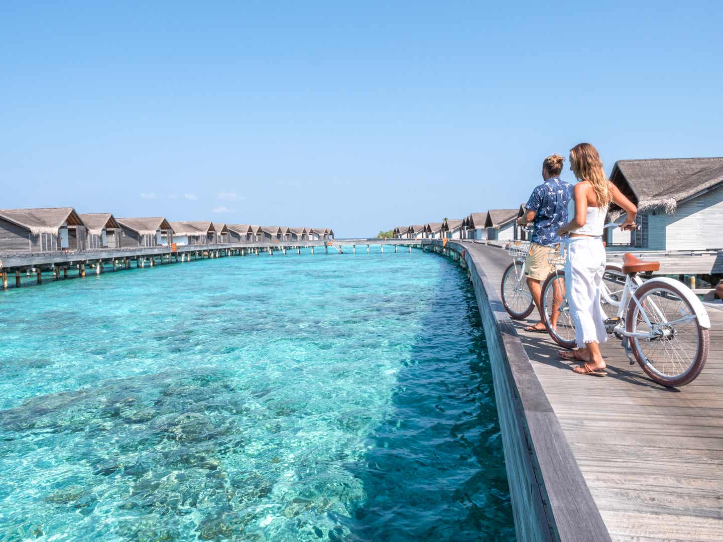 Ein Paar genießt die Aussicht auf das klare Wasser der Malediven von einem Holzsteg zwischen luxuriösen Wasserbungalows