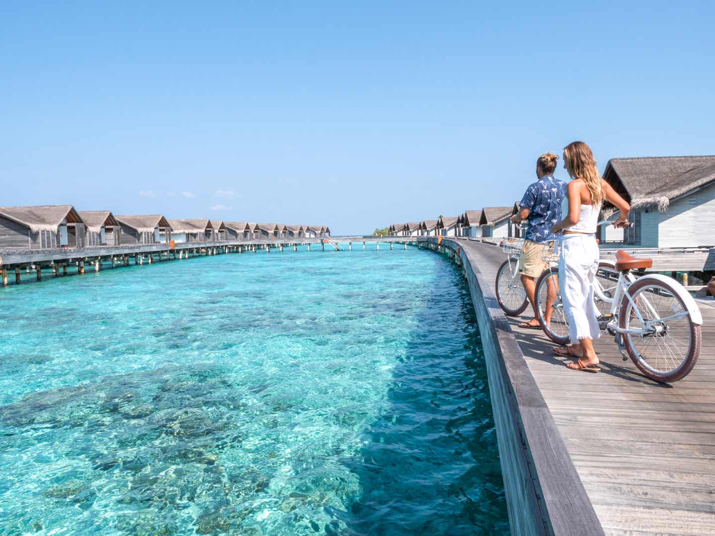 Ein Paar genießt die Aussicht auf das klare Wasser der Malediven von einem Holzsteg zwischen luxuriösen Wasserbungalows