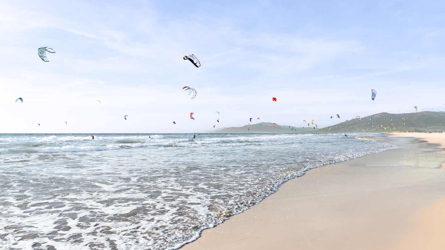 Kitesurfer und bunte Kites über dem Playa de Los Lances in Tarifa bei Sonnenschein und klarer Sicht 