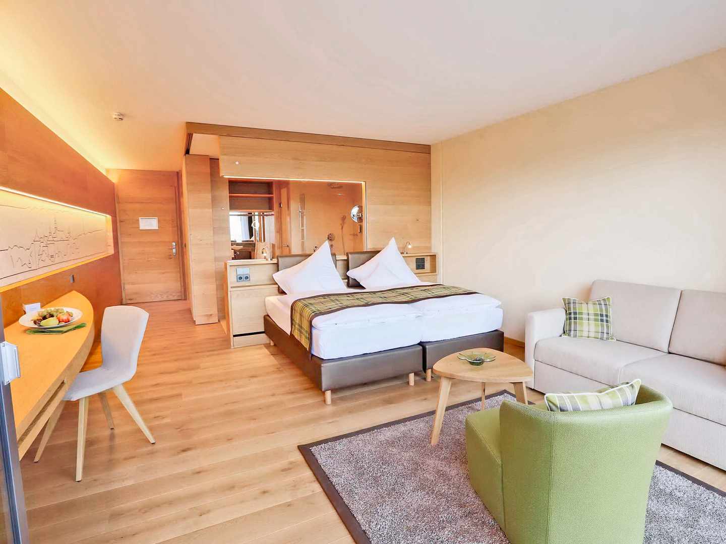 Offen geschnittener Wohn- und Schlafbereich – kurze Wege, klare Struktur und viel Platz zum Ankommen Zimmer im Mawell Resort Langenburg mit Doppelbett, Sitzecke und hellem Holzdesign