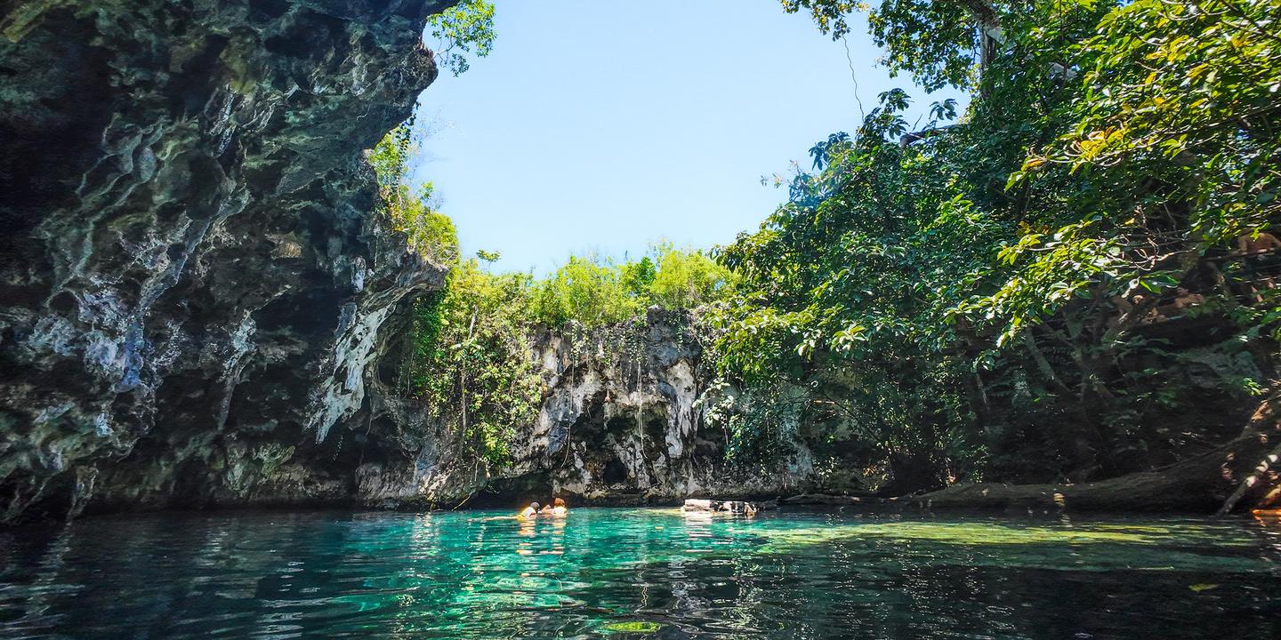 Natürliche Lagune auf Sansibar mit türkisfarbenem Wasser, Felswänden und üppiger Vegetation bei einem Sansibar-Ausflug ins Inselinnere.