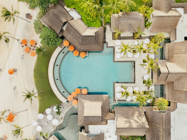 Top-Shot einer Drohne mit zentraler Poolanlage, Sonnenliegen, Unterkünften und Strand