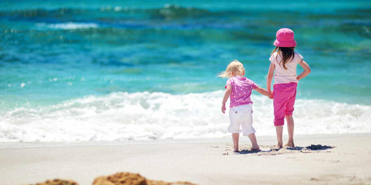 Zwei kleine Mädchen in Pink und Lila stehen Hand in Hand am Ufer des Meeres