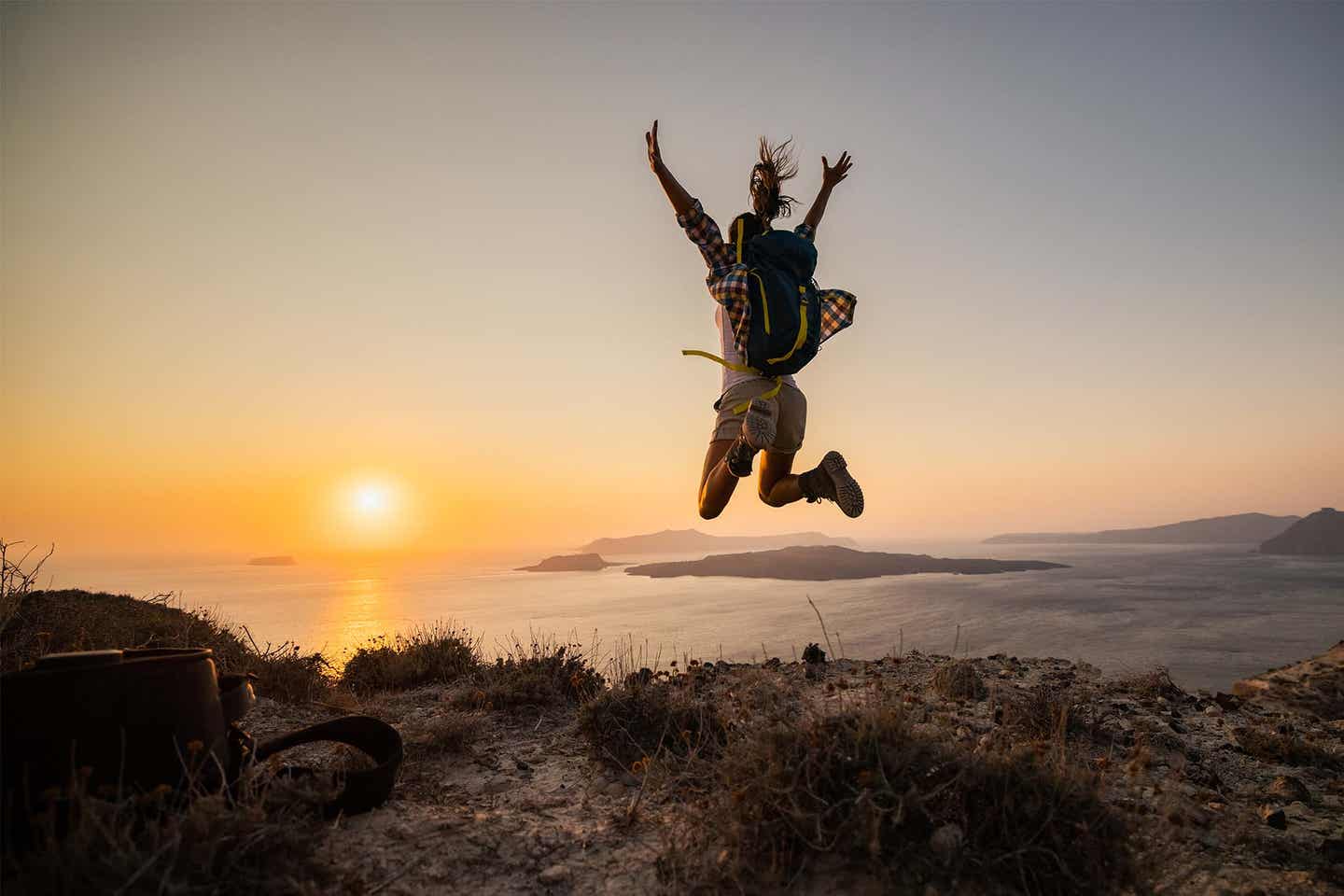 Wanderer springt auf einer Klippe am Meer in Sonnenuntergang auf Santorini