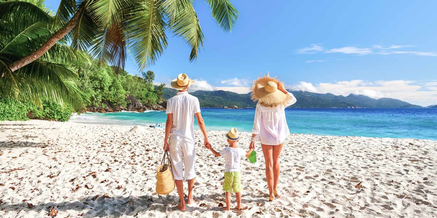 Familie mit Mutter, Vater und Kind im Mahé-Urlaub am hellen Sandstrand, gesäumt von Palmen und Bergen