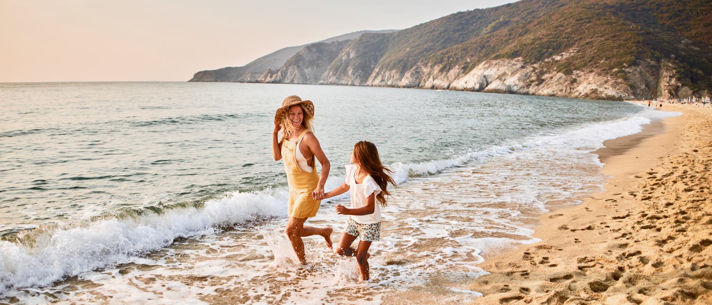 Mutter und Tochter laufen an einem griechischen Strand durchs Wasser