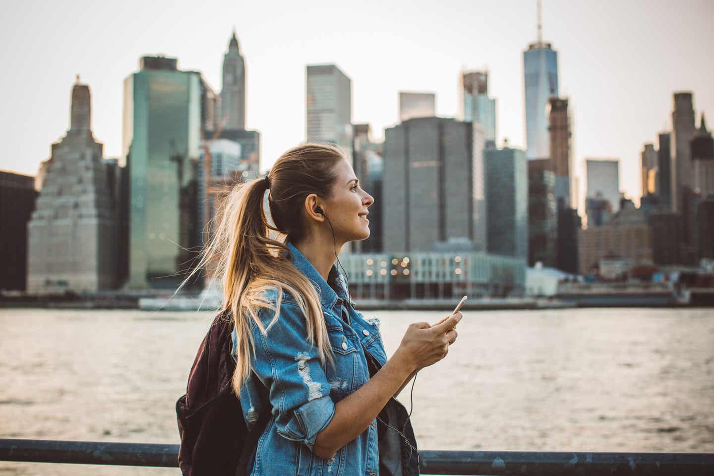 Frau hört Musik am Wasser mit Skyline im Hintergrund