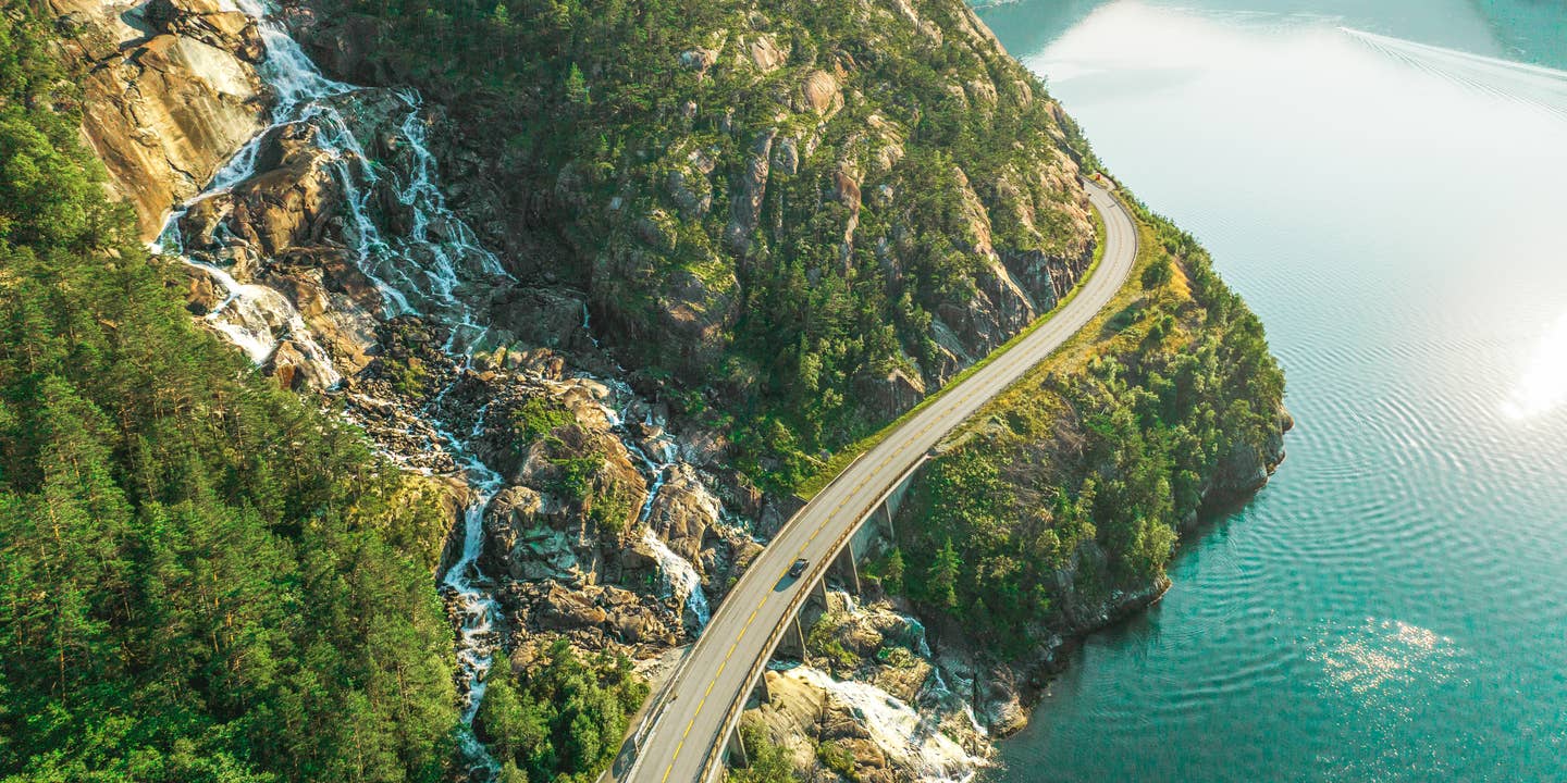 Eine Rundreise durch Norwegen aus der Vogelperspektive: Ein Auto fährt auf einer Straße entlang eines Fjords Eine Rundreise durch Norwegen aus der Vogelperspektive: Ein Auto fährt auf einer Straße entlang eines Fjords