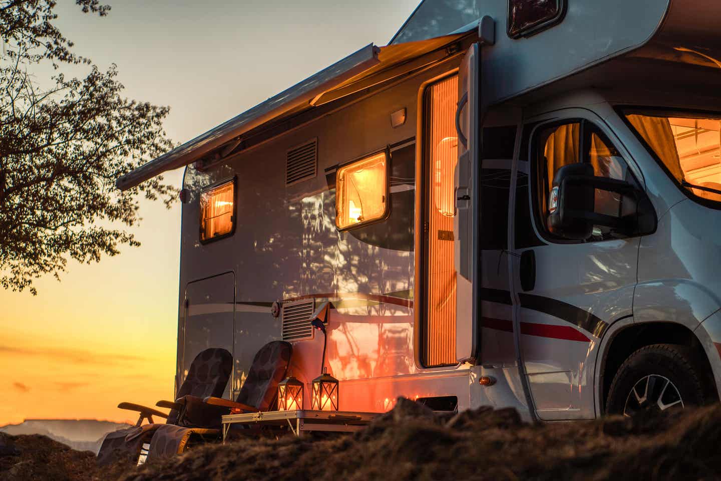 Camper mit zwei Stühlen und Kerzen beim Sonnenuntergang