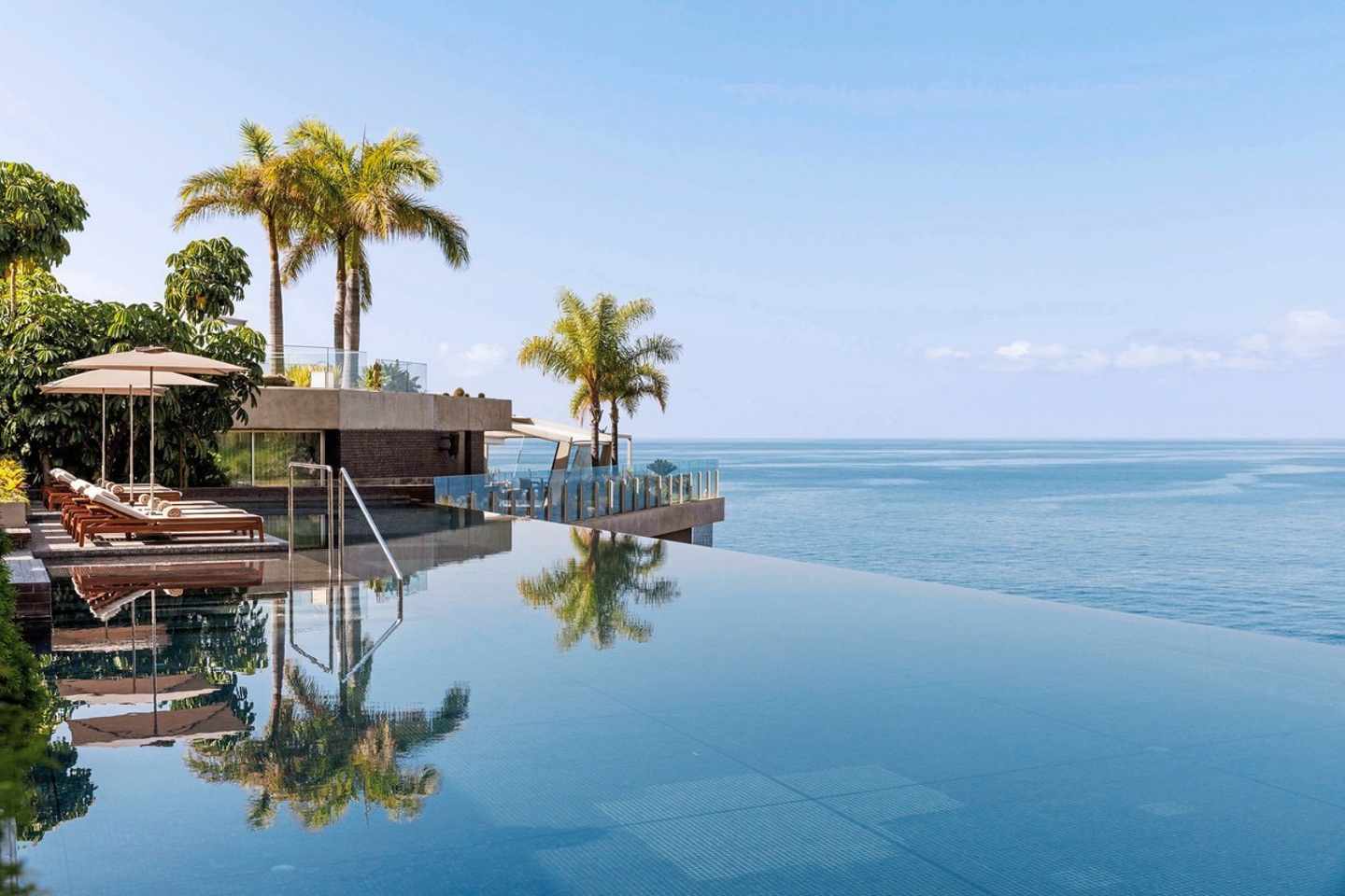 Blick auf den Infinitypool im Saccharum Resort auf Madeira, dahinter das Meer, Palmen und Liegen zur linken Seite des Pools