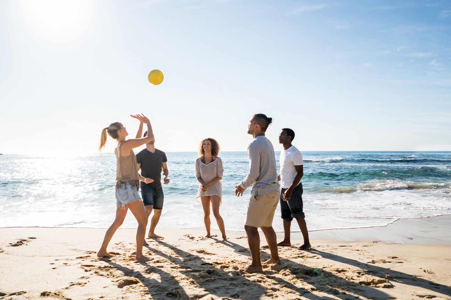 Junge Menschen spielen am sonnigen Strand Volleyball