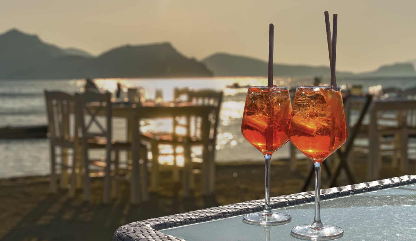 Italienische Adria Urlaub mit DERTOUR. Restaurant am Meer bei Sonnenuntergang. Zwei Gläser Aperol Spritz auf einem Tisch