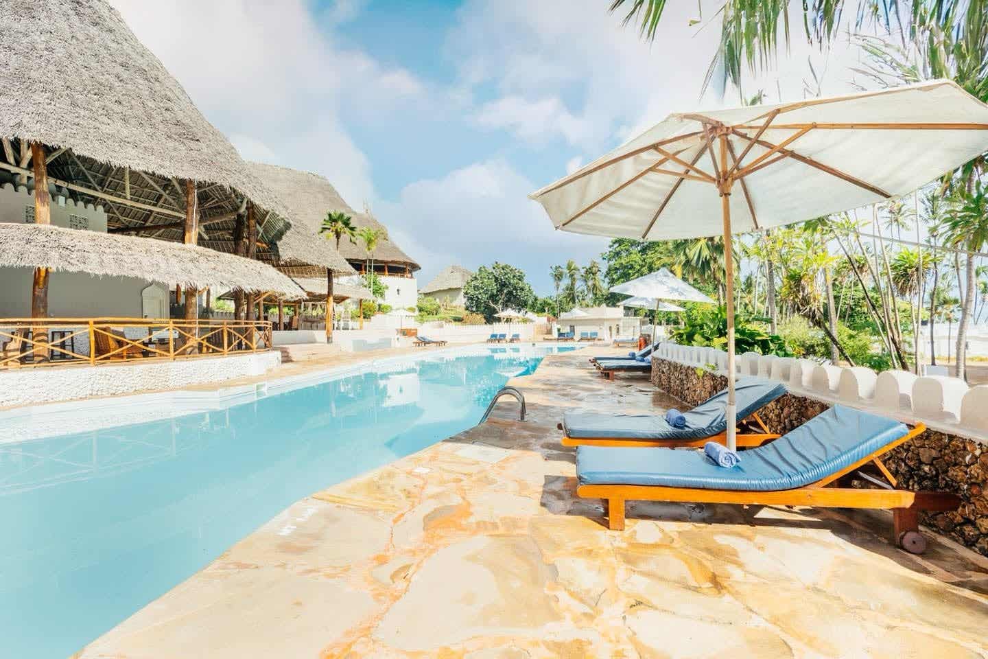 Entspannung am Pool des ananea Diamonds Mapenzi in Kiwengwa Poolbereich im ananea Diamonds Mapenzi Resort in Kiwengwa, Sansibar mit Sonnenliegen, Palmen und Makuti-Dächern in tropischer Umgebung