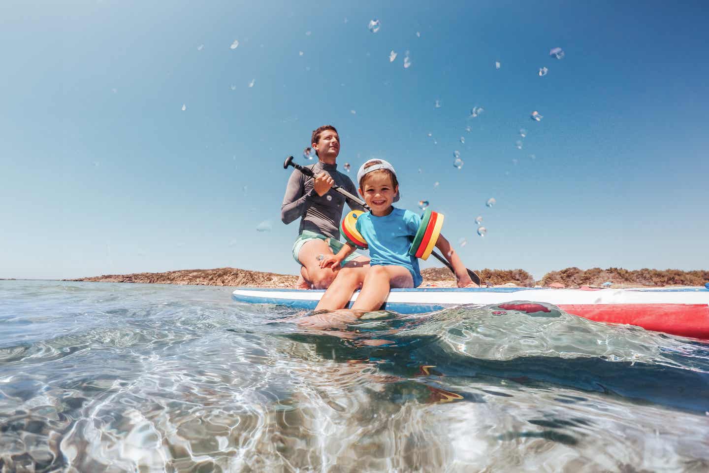 Sardinien Urlaub mit DERTOUR. Vater und Sohn spielen im Wasser des Mittelmeers bei Sonnenuntergang