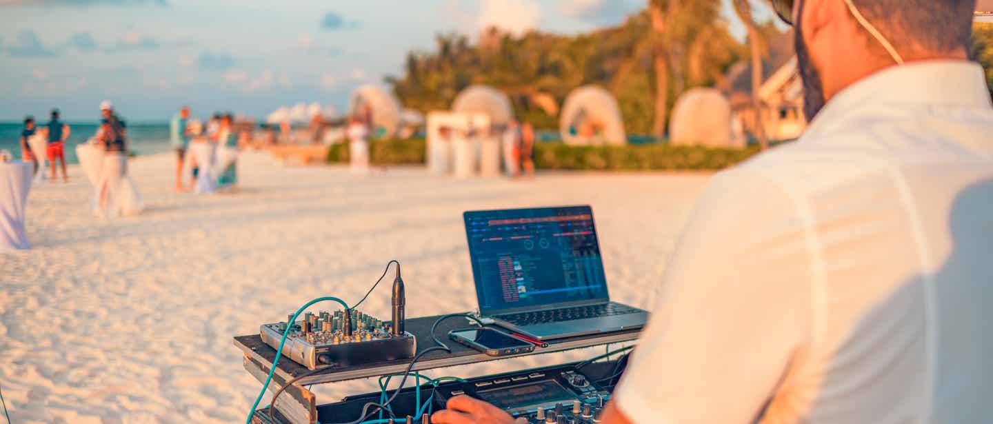 DJ mit Mischpult bei Sonnenuntergang am Strand bei einer Sunset-Beach-Party im Sommerurlaub