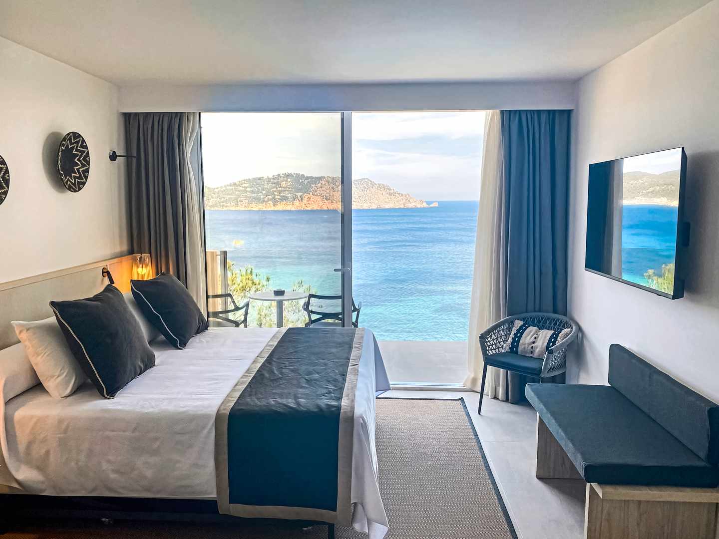 Zimmer im Sentido Cala Verde auf Ibiza mit Doppelbett, Sitzmöbeln, Wand-TV und Panoramafenster mit Blick auf das Mittelmeer