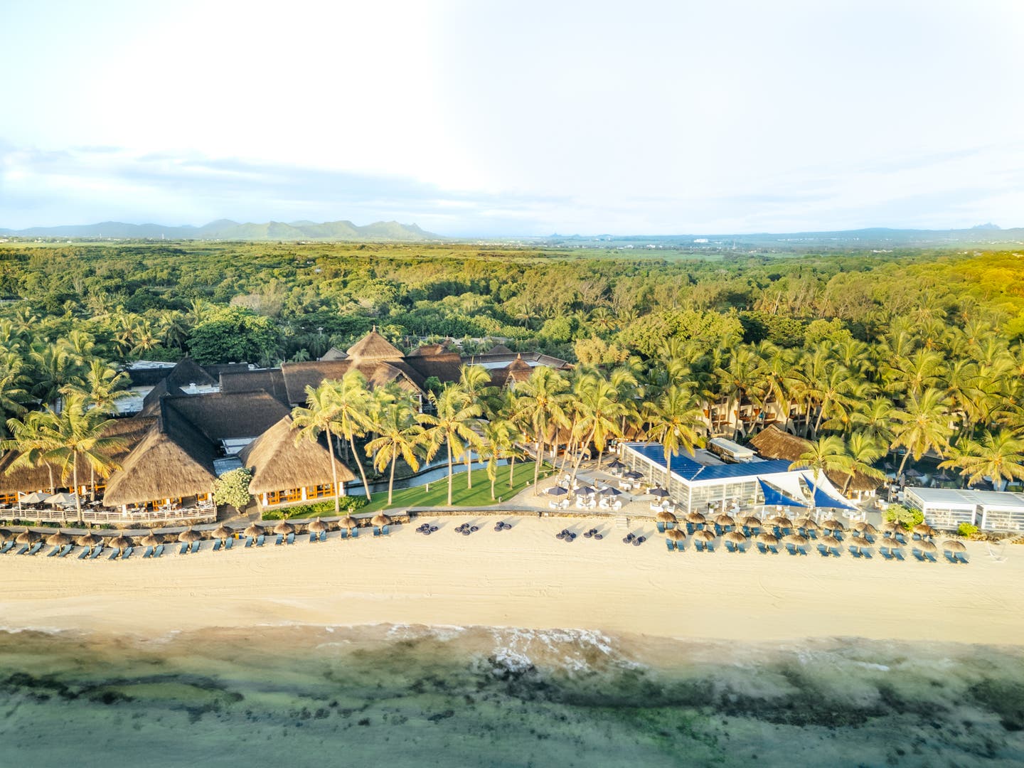 Luftaufnahme mit Strand, Hotelanlage und der grünen Insel im Hintergrund
