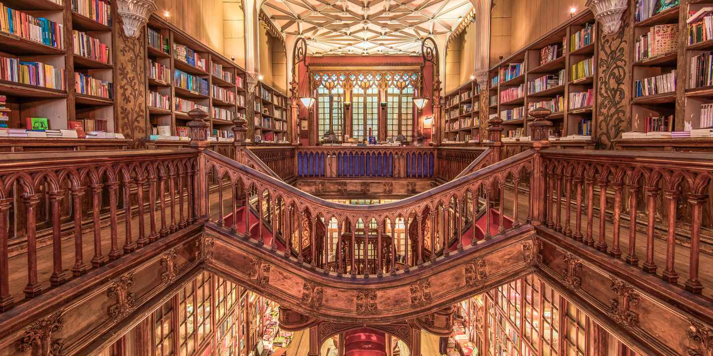 Innenansicht der Livraria Lello in Porto mit Holztreppe, Bücherregalen und verziertem Glasdach