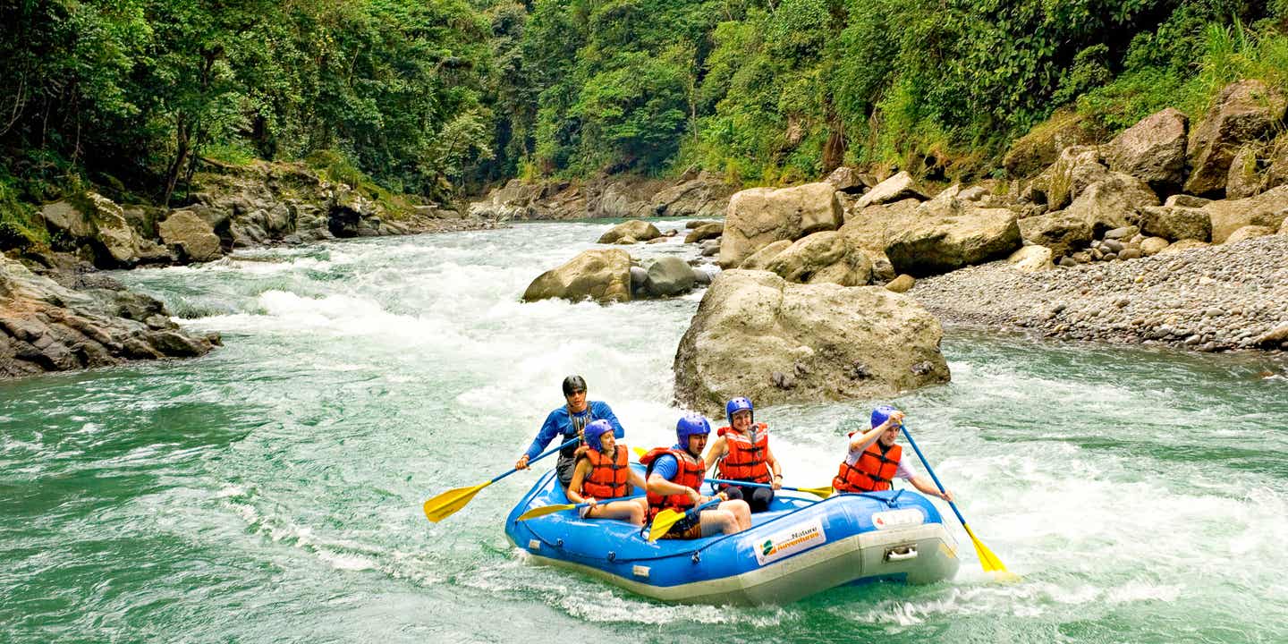 Ein Rafting-Boot mit fünf Insassen schwimmt auf einem Fluss in Costa Rica, im Hintergrund der Regenwald 