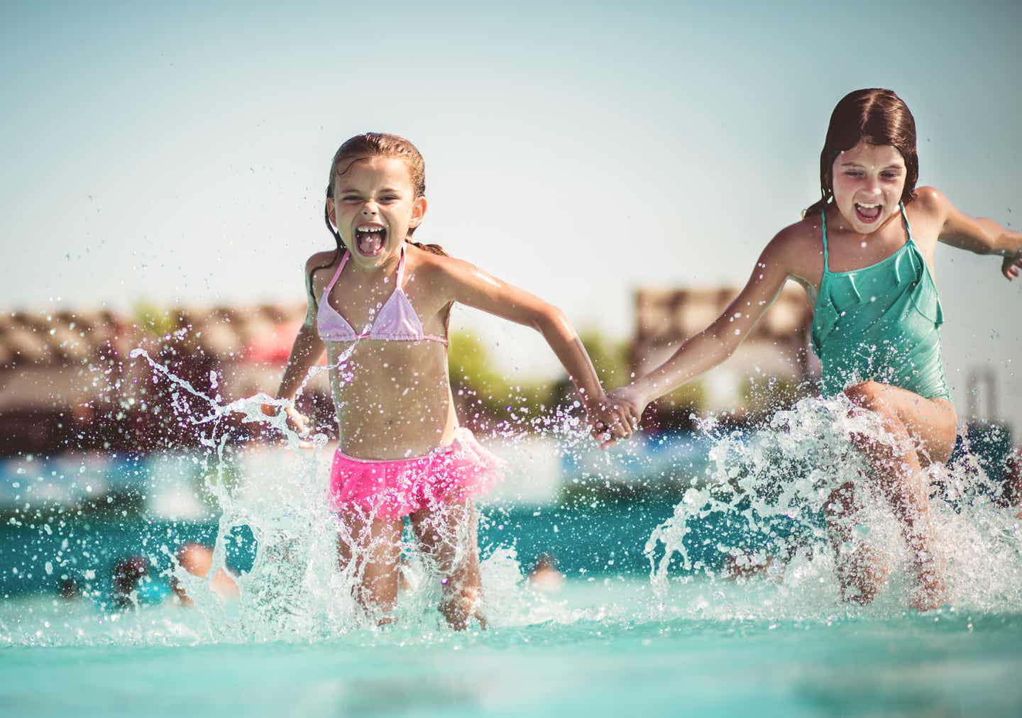 Zwei Mädchen rennen Hand in Hand durch das Wasser eines Pools