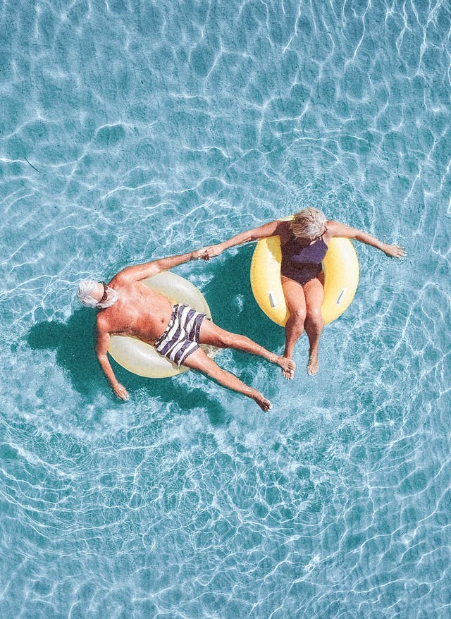 Langzeiturlaub für Senioren Ein Seniorenpaar schwimmt auf Schwimmreifen im Meer.