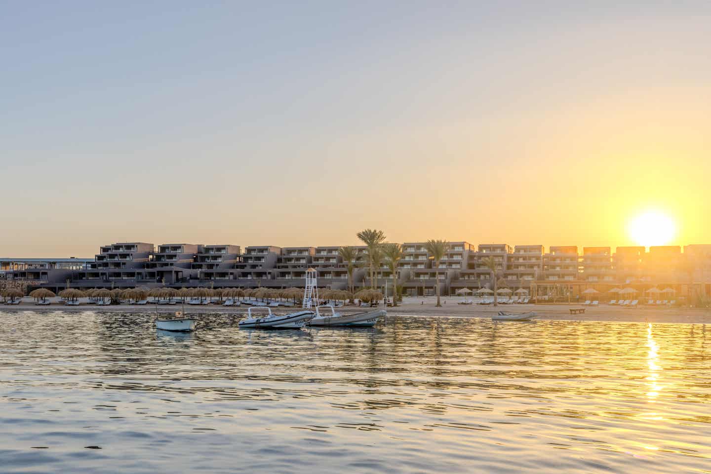 Sonnenuntergang über dem Aldiana Club Naga Bay direkt am Roten Meer mit Booten und Palmen am Strand